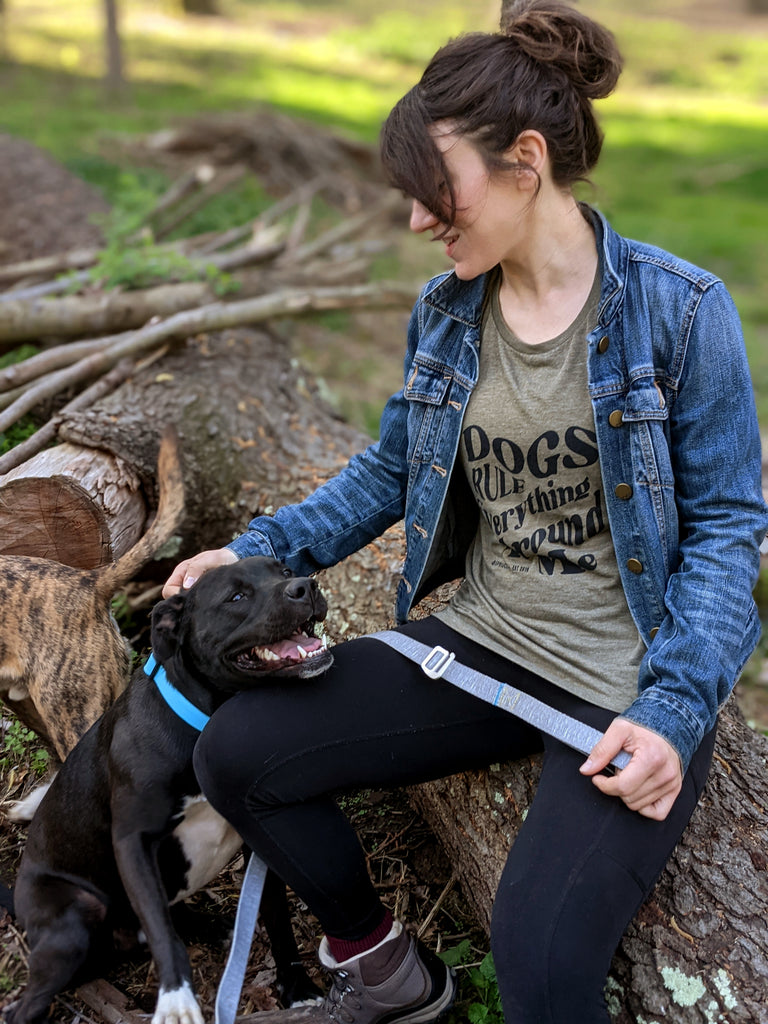 Woman wearing 'Dogs Rule Everything Around Me' tank top sitting next to her dog on a log